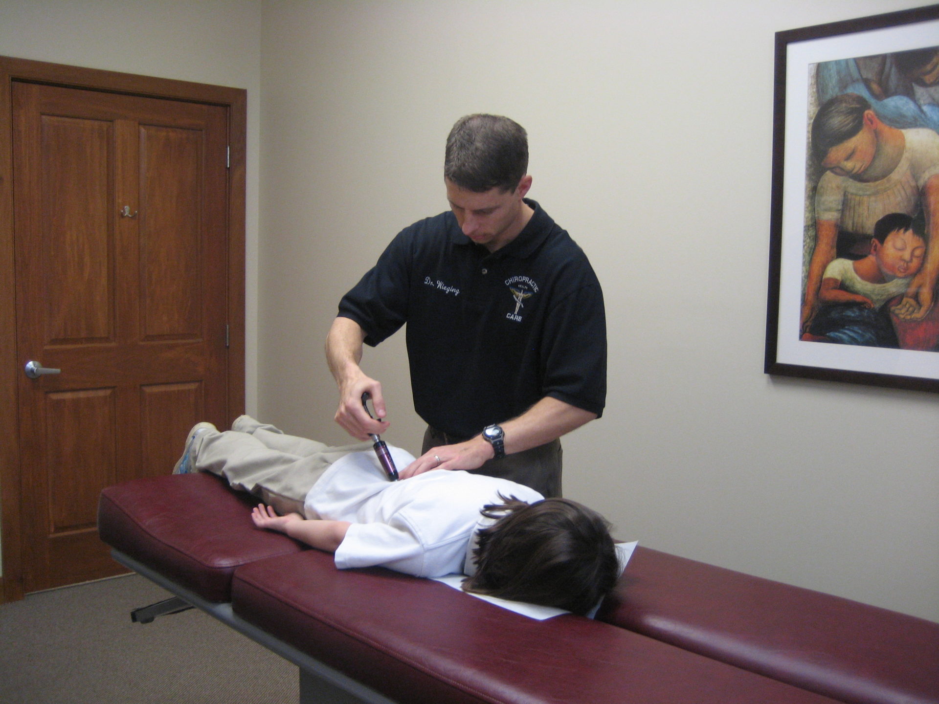 A child lying on a chiropractic table while a chiropractor adjusts his back.